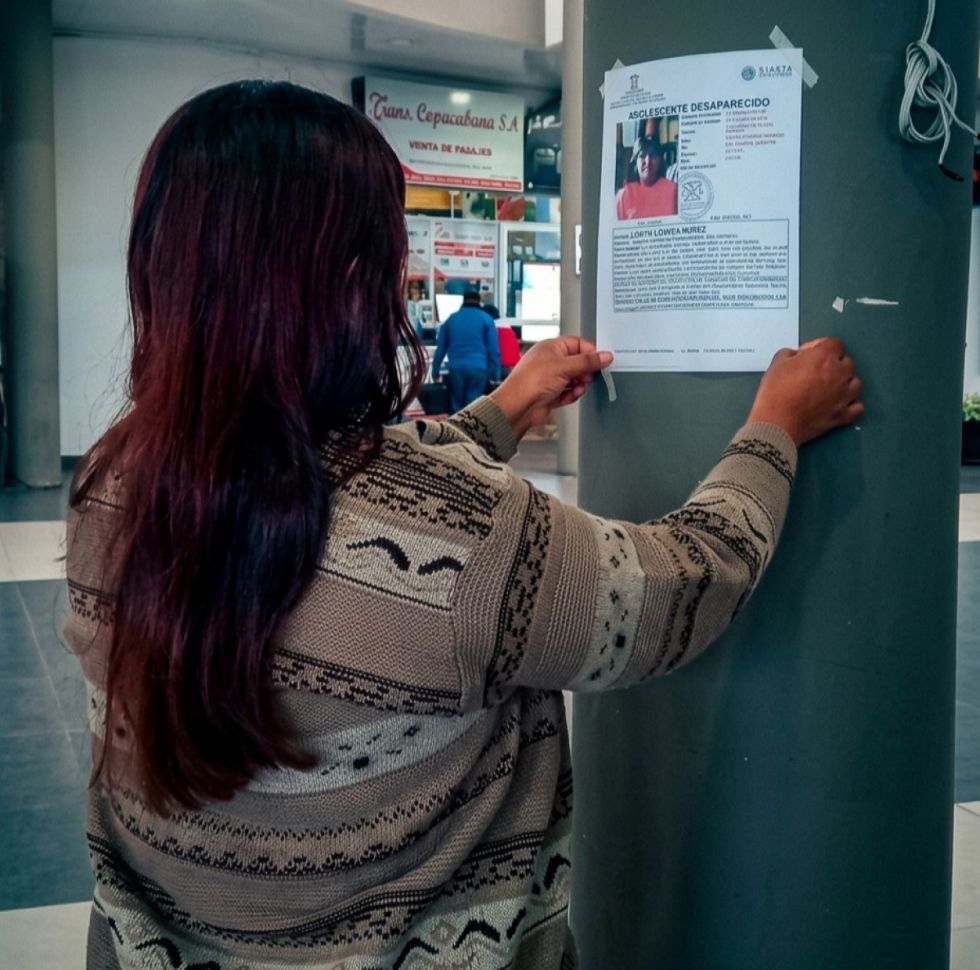 Una mujer pega un cartel buscando a un familiar en la terminal de buses de Tarija
